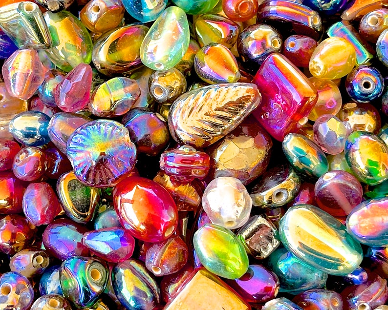 K&ouml;nnte beinhalten: Eine Sammlung von irisierenden Glasperlen in verschiedenen Formen und Gr&ouml;&szlig;en, darunter runde, ovale und blattartige Perlen. Die Perlen sind in einer Mischung aus Farben, darunter Gold, Rot, Lila, Blau und Gr&uuml;n.