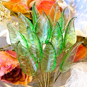 May include: A bouquet of green glass leaves with a textured surface. The leaves are arranged in a fan shape and are attached to gold-colored stems.