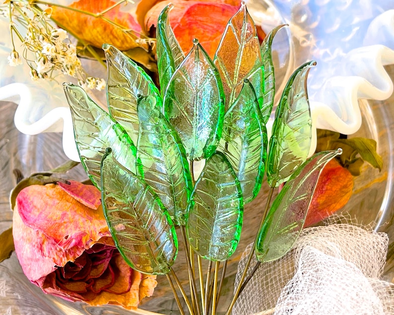 May include: A bouquet of green glass leaves with a textured surface. The leaves are arranged in a fan shape and are attached to gold-colored stems.