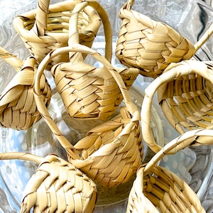 May include: A group of small, woven baskets with handles. The baskets are made of natural materials and have a light brown color.
