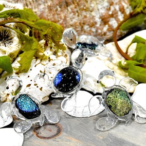 May include: Three glass sea turtle figurines with iridescent shells. The turtles are clear glass with a black, blue, and green iridescent finish.