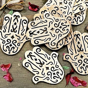 May include: A set of wooden hand-shaped ornaments with intricate black designs. The ornaments are made of light brown wood and have a natural finish.