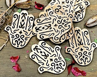 Può includere: Un set di ornamenti in legno a forma di mano con intricati disegni neri. Gli ornamenti sono realizzati in legno marrone chiaro e hanno una finitura naturale.