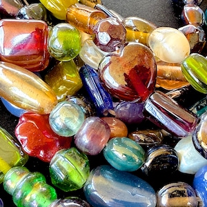 May include: A collection of colorful glass beads in various shapes and sizes. The beads are in shades of red, green, yellow, blue, and purple. Some beads are heart-shaped, while others are rectangular or oval.