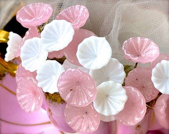 May include: A bouquet of pink and white glass flowers with a delicate, ruffled texture. The flowers are arranged in a vase with a pink and gold design.