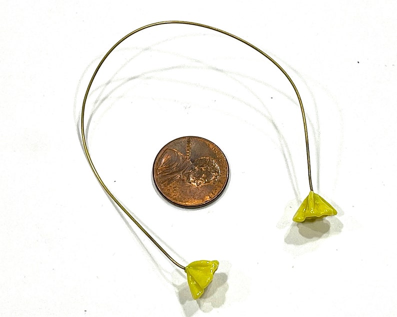 May include: A pair of yellow flower-shaped charms attached to a thin gold wire.