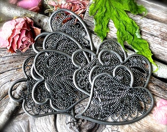 Può includere: Un set di cinque cuori in metallo nero con intricati disegni ritagliati. I cuori sono sovrapposti, creando un effetto tridimensionale.