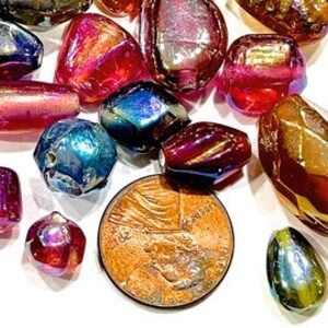 K&ouml;nnte beinhalten: Sortiment an regenbogenfarbenen Glasperlen in verschiedenen Formen und Gr&ouml;&szlig;en, darunter runde, ovale und facettierte. Die Perlen sind in Rot-, Blau-, Gr&uuml;n- und Goldt&ouml;nen gehalten. Ein Cent-St&uuml;ck ist zur Gr&ouml;&szlig;enbestimmung enthalten.