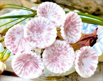 May include: A cluster of seven white glass flowers with pink speckles. The flowers are arranged in a bowl and have a delicate, ruffled appearance.