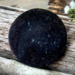 May include: A black circular watch back with a small hole in the center and scratches on the surface.