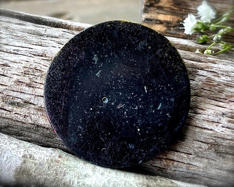 May include: A black circular watch back with a small hole in the center and scratches on the surface.