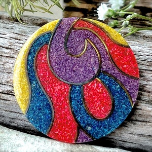 May include: A round, colorful, decorative object with a swirling pattern of red, blue, yellow, and purple. The object is made of small, textured pieces that create a mosaic-like effect.