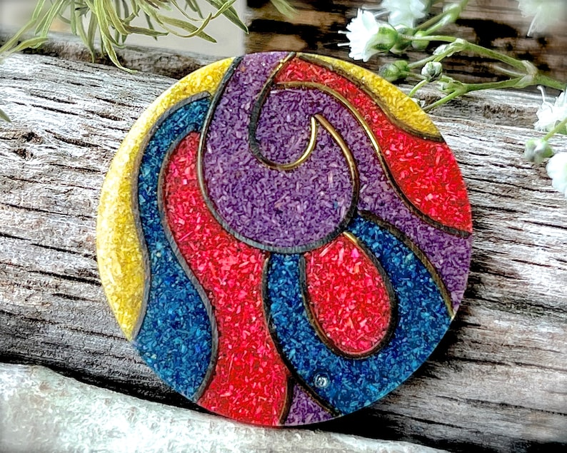 May include: A round, colorful, decorative object with a swirling pattern of red, blue, yellow, and purple. The object is made of small, textured pieces that create a mosaic-like effect.