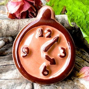 May include: A brown ceramic clock with a white face and black numbers. The clock is shaped like a circle and has a brown rim.