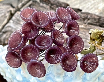 May include: A cluster of purple glass flowers with a ruffled texture. The flowers are arranged in a bouquet-like shape and appear to be made of blown glass.