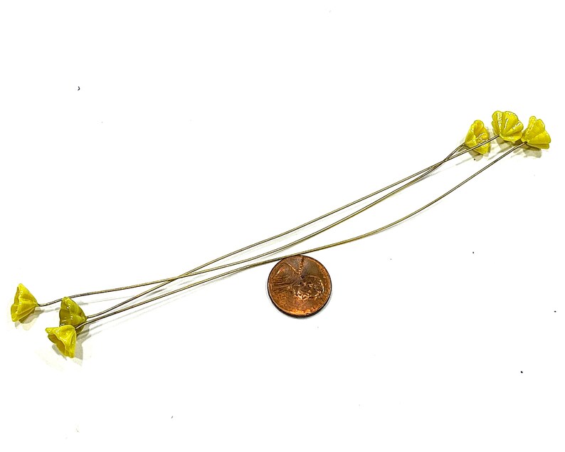 May include: Five yellow flower stems with wire stems. The stems are arranged in a fan shape and are about the size of a UK penny.