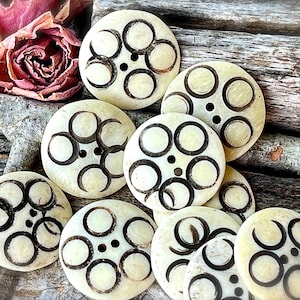 May include: A collection of eight white bone buttons with a black triple moon design. The buttons are round and have a raised edge.