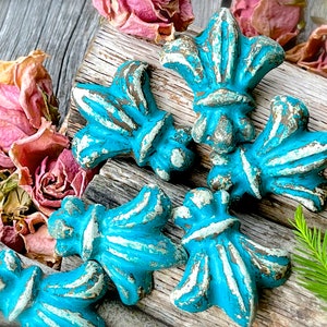 May include: Six turquoise blue and white fleur-de-lis shaped decorative ornaments with a distressed finish.