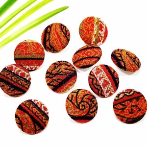 May include: Ten round fabric buttons with a variety of colorful patterns in shades of orange, red, black, and white. The buttons are approximately 1 inch in diameter.