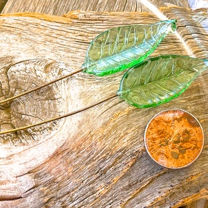 May include: Two green glass leaves on wire stems. The leaves are on a wooden surface with a copper penny.