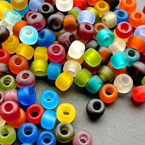 Puede incluir: Una colección de cuentas de vidrio de colores en varios tonos de azul, verde, rojo, amarillo, naranja y morado. Las cuentas son redondas y tienen un acabado liso y brillante.