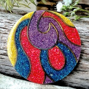 May include: A round, colorful, decorative object with a swirling pattern in shades of red, yellow, blue, and purple. The object is made of a textured material that resembles small, colorful pebbles.