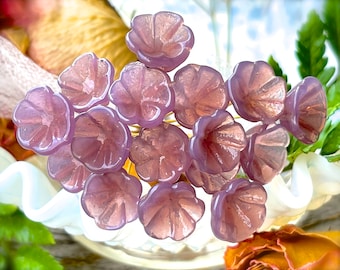 Könnte beinhalten: Eine Sammlung von 14 lila Glasblumenperlen. Die Perlen sind in Form einer Blume mit einem gekräuselten Rand geformt. Sie sind perfekt für die Schmuckherstellung oder andere Bastelprojekte.