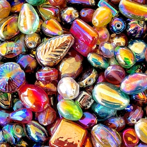 K&ouml;nnte beinhalten: Eine Sammlung von irisierenden Glasperlen in verschiedenen Formen und Gr&ouml;&szlig;en, darunter Tropfen-, Oval- und Rundformen. Die Perlen haben einen regenbogenartigen Glanz und eignen sich perfekt f&uuml;r die Schmuckherstellung oder das Basteln.