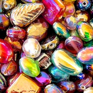K&ouml;nnte beinhalten: Eine Auswahl an irisierenden Glasperlen in verschiedenen Formen und Gr&ouml;&szlig;en, darunter ovale, runde und blattf&ouml;rmige Perlen. Die Perlen sind eine Mischung aus Rot, Gold, Gr&uuml;n und Blau.