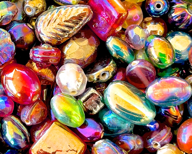 K&ouml;nnte beinhalten: Eine Auswahl an irisierenden Glasperlen in verschiedenen Formen und Gr&ouml;&szlig;en, darunter ovale, runde und blattf&ouml;rmige Perlen. Die Perlen sind eine Mischung aus Rot, Gold, Gr&uuml;n und Blau.