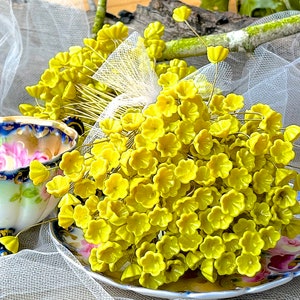 May include: A bunch of small, bright yellow flower-shaped embellishments on wire stems. The embellishments are clustered together and arranged on a white lace fabric background.