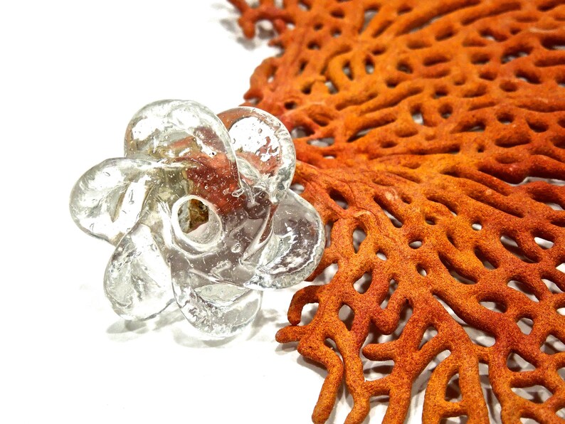 Peut inclure: Un objet en verre souffl&eacute; transparent en forme de fleur &agrave; plusieurs p&eacute;tales tourbillonnants avec une ouverture circulaire centrale, pr&eacute;sentant de petites bulles d'air internes dans tout le verre, plac&eacute; &agrave; c&ocirc;t&eacute; d'un grand corail &eacute;ventail orange.