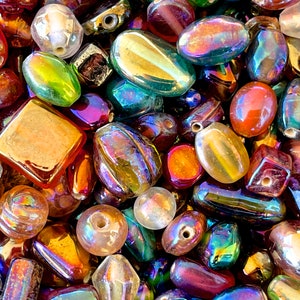K&ouml;nnte beinhalten: Eine Sammlung von irisierenden Glasperlen in verschiedenen Formen und Gr&ouml;&szlig;en, darunter ovale, quadratische und runde. Die Perlen sind in verschiedenen Farben, darunter Rot, Gr&uuml;n, Blau und Gold.