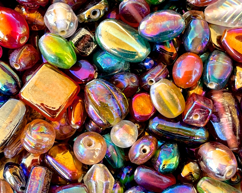 K&ouml;nnte beinhalten: Eine Sammlung von irisierenden Glasperlen in verschiedenen Formen und Gr&ouml;&szlig;en, darunter ovale, quadratische und runde. Die Perlen sind in verschiedenen Farben, darunter Rot, Gr&uuml;n, Blau und Gold.