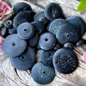 Peut inclure: Un ensemble de perles en bois noires en forme de disque avec un trou au centre. Les perles sont disposées en pile sur une surface en bois.