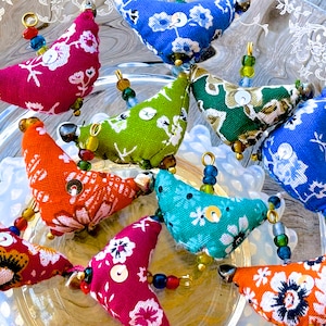 May include: A collection of eight colorful fabric bird ornaments with beaded strings. Each ornament features a different floral pattern and a button accent.