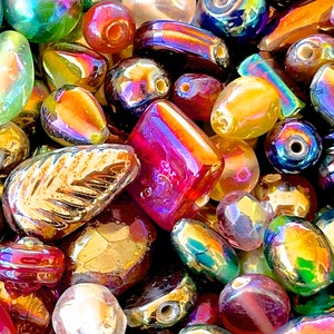 K&ouml;nnte beinhalten: Eine Sammlung von irisierenden Glasperlen in verschiedenen Formen und Gr&ouml;&szlig;en, darunter runde, ovale und blattf&ouml;rmige Perlen. Die Perlen sind in einer Mischung aus Farben, darunter Rot, Orange, Gelb, Gr&uuml;n, Blau und Lila.