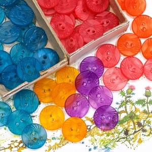 May include: Assortment of colorful plastic buttons with a geometric design. The buttons are in shades of blue, purple, orange, and pink.