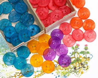 May include: Assortment of colorful plastic buttons with a geometric design. The buttons are in shades of blue, purple, orange, and pink.