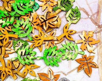 Op de afbeelding: Assortiment van houten bladeren in groene en oranje tinten. De bladeren zijn uitgesneden en hebben een rustieke, verweerde uitstraling.