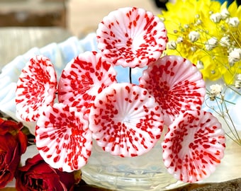 May include: A cluster of six white glass flowers with red speckles. The flowers are arranged in a circular pattern and have a delicate, ruffled appearance.