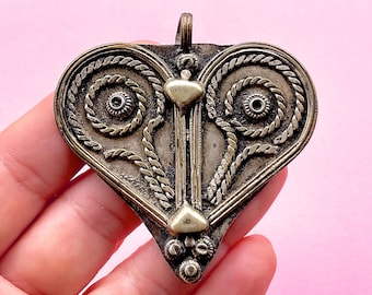 Puede incluir: Un colgante de corazón de plata con detalles intrincados y un acento dorado en el centro. El colgante tiene un diseño de cuerda alrededor de los bordes y un patrón de espiral a cada lado.