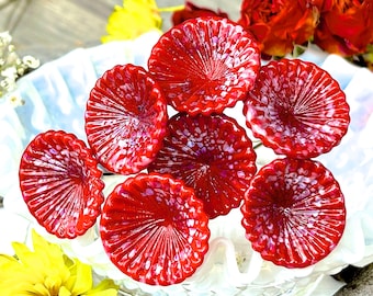 May include: A cluster of seven red and white glass flower-shaped ornaments with a white background.
