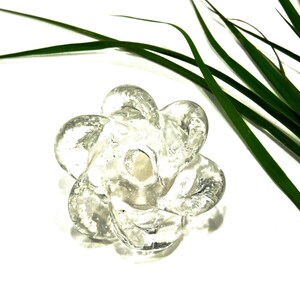 Peut inclure: Un objet en verre transparent et incolore en forme de fleur &agrave; six p&eacute;tales. Le verre pr&eacute;sente un aspect textur&eacute; et organique avec des bulles internes visibles et une surface lisse et arrondie. Le centre de la fleur comporte une petite indentation.