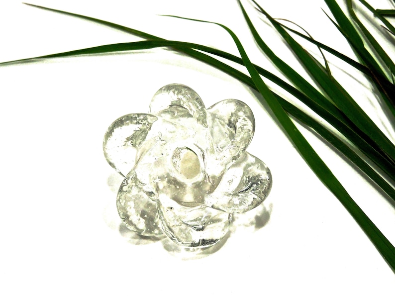 Peut inclure: Un objet en verre transparent et incolore en forme de fleur &agrave; six p&eacute;tales. Le verre pr&eacute;sente un aspect textur&eacute; et organique avec des bulles internes visibles et une surface lisse et arrondie. Le centre de la fleur comporte une petite indentation.