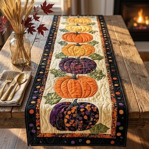 Peut inclure: Un chemin de table matelassé rectangulaire présentant une rangée verticale de six citrouilles dans des tons orange, jaune et violet avec des motifs floraux, sur un fond crème avec des feuilles vertes, bordé d'une bordure noire à pois colorés.