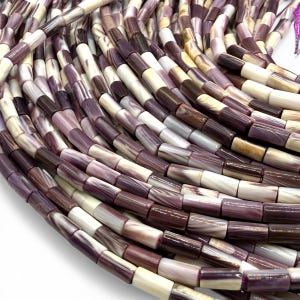 May include: Close-up of a collection of rectangular beads in shades of purple, brown, and cream. The beads are strung together, creating a textured and layered effect. Ideal for jewelry making or crafting projects.
