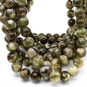 May include: A collection of round, green beads with varying shades and patterns. The beads have a polished, glossy appearance and are strung together, suggesting they are for jewellery making or crafting. The beads are on a white background.