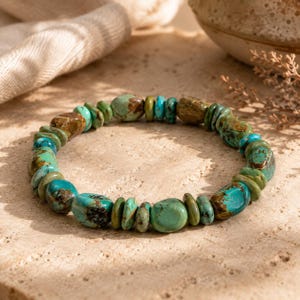 May include: A stretch bracelet composed of irregular, tumbled beads in shades of turquoise blue, sage green, and earthy brown. The beads vary in size and shape, featuring natural matrix patterns and smooth, polished surfaces arranged in a circular loop.