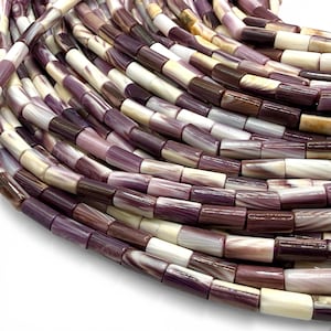 May include: Close-up of a collection of cylindrical beads in shades of purple, cream, and brown. The beads have a glossy finish and are arranged in a curved pattern, suggesting they are part of a larger strand or design. The beads are approximately 0.5 inches long.